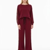 Model wearing a burgundy lounge set with leopard-print side stripes and white sneakers, full-body pose in a studio.