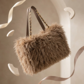 Brown fluffy handbag with a gold chain strap suspended among curling ribbons in a neutral studio setting, showcasing its plush texture.