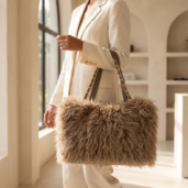 Woman in a cream suit carries a large fluffy beige handbag with a gold chain strap in a sunlit boutique.