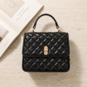 Black quilted handbag with a gold clasp and top handle on a light countertop, with magazines nearby.