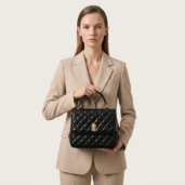 Woman in a tan tailored suit holding a black quilted handbag with a gold clasp.