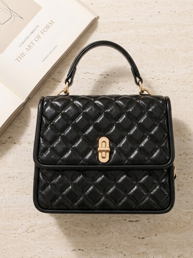 μαυρη τσαντα Black quilted handbag with a gold clasp and top handle on a light countertop, with magazines nearby.
