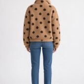 Person wearing a tan teddy coat with black polka dots, blue jeans, and white sneakers, viewed from the back against a plain backdrop