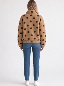 Person wearing a tan teddy coat with black polka dots, blue jeans, and white sneakers, viewed from the back against a plain backdrop