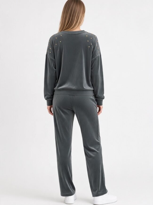 Velvet Γκρί 2 Person standing with back to camera, wearing a dark gray velour tracksuit with gold stud accents on the shoulders and white sneakers.