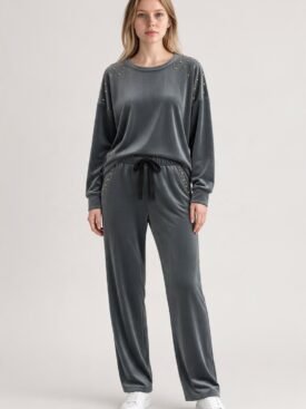 Gray velour tracksuit with gold stud embellishments on shoulders and pockets, a black drawstring waist, and white sneakers on a standing model, fashion photo.
