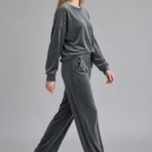 Woman walking in a grey velour tracksuit with studded shoulders and white sneakers, posing against a neutral background.
