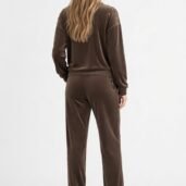 Woman wearing a brown velour tracksuit seen from behind, with gold studs on the shoulders and side, and white sneakers.