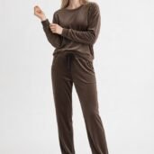 Model wearing a brown velour tracksuit with stud embellishments and white sneakers, posing in a studio light backdrop