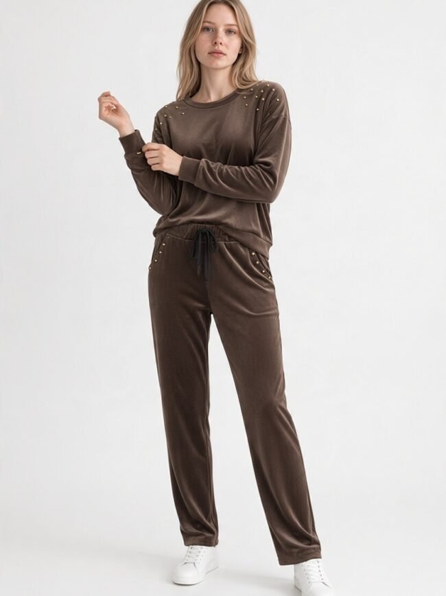 Velvet Καφέ 2 Model wearing a brown velour tracksuit with stud embellishments and white sneakers, posing in a studio light backdrop