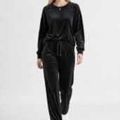 Front view of a woman wearing a black velour tracksuit with gold studs on the shoulders and pockets, paired with white sneakers.