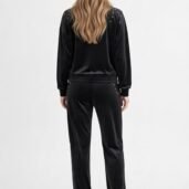 Back view of a person in a black velour tracksuit with gold studs on the shoulders and pockets, wearing white sneakers.