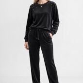 Full-body shot of a model in a black velour tracksuit with stud embellishments and white sneakers, standing with hands in pockets.