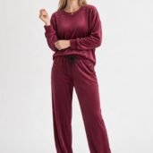 Woman wearing burgundy velour loungewear with studded shoulders, standing against a light background.