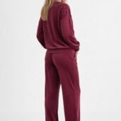 Back view of a woman in a burgundy velour tracksuit with studded shoulders and white sneakers.