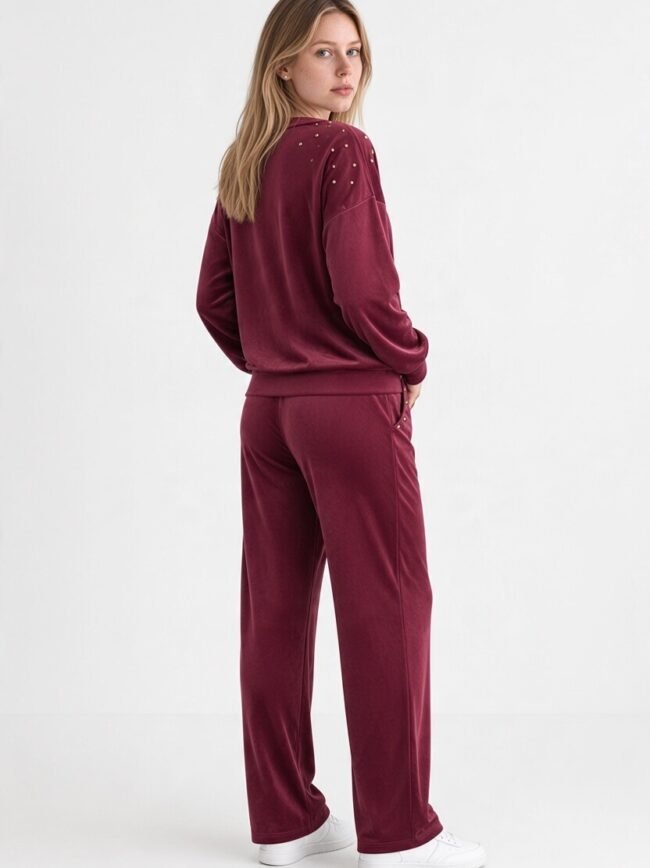 Velvet Μπορντό 2 Back view of a woman in a burgundy velour tracksuit with studded shoulders and white sneakers.