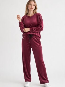 Woman wearing burgundy velour loungewear with studded shoulders, standing against a light background.
