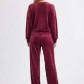 Back view of a woman wearing a burgundy velour tracksuit with small studs on the shoulders and sides.