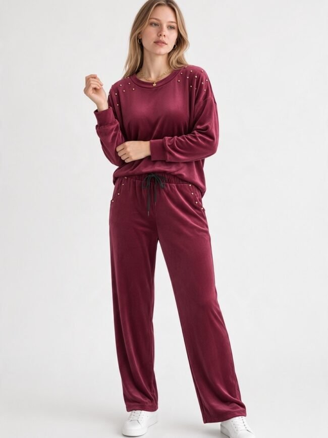Velvet Μπορντό Woman wearing burgundy velour loungewear with studded shoulders, standing against a light background.