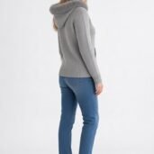 Woman in a light gray knit hoodie with fur-trimmed hood, blue jeans, and white sneakers, standing in a side-facing pose.
