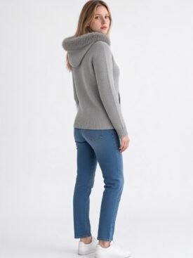 Woman in a light gray knit hoodie with fur-trimmed hood, blue jeans, and white sneakers, standing in a side-facing pose.