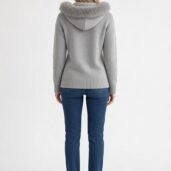 Back view of a person wearing a light gray hooded sweater with a fluffy fur-trimmed hood, blue jeans, and white sneakers