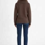 Back view of a person wearing a brown chunky knit sweater with a fur collar, blue jeans, and white sneakers against a white background.