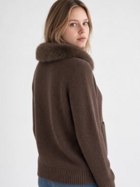 Woman wearing a brown knit sweater with a fur collar, looking over her shoulder at the camera.