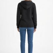 Back view of a person wearing a black hooded sweater with blue jeans and white sneakers, standing against a light background.