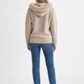 Back view of a person wearing a beige hooded sweater with a fluffy fur trim, blue jeans, and white sneakers.