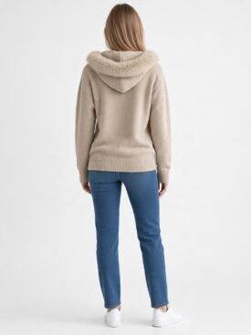 Back view of a person wearing a beige hooded sweater with a fluffy fur trim, blue jeans, and white sneakers.