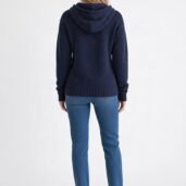 Back view of a person wearing a navy knit hoodie and blue jeans, white sneakers, standing against a white background