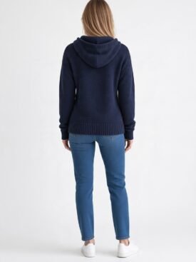 Back view of a person wearing a navy knit hoodie and blue jeans, white sneakers, standing against a white background
