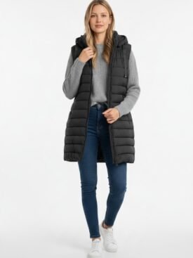 Woman wearing a long black quilted puffer vest over a gray knit sweater, blue jeans, and white sneakers.