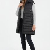Woman in a knee-length black puffer vest with hood over a light gray knit sweater, dark jeans, and white sneakers.