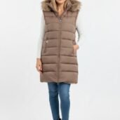 Woman wearing a knee-length brown puffer vest with a fur-trimmed hood over a white knit sweater, blue jeans, and black ankle boots.