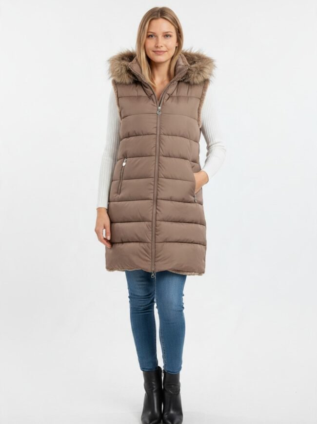Woman wearing a knee-length brown puffer vest with a fur-trimmed hood over a white knit sweater, blue jeans, and black ankle boots.