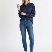 Woman modeling a navy button-down shirt with blue jeans and white sneakers against a white background.