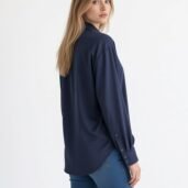 Woman with long blonde hair wearing a navy button-up shirt and blue jeans, facing slightly away from the camera.