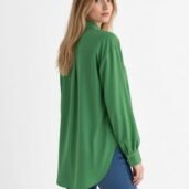 Back view of a woman wearing a green long-sleeve blouse with a curved hem, paired with blue jeans.