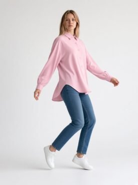 Model wearing a pink oversized button-down shirt with blue jeans and white sneakers, posing mid-step against a light background.