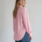 Woman with long blonde hair wearing a pink button-down blouse and blue jeans, turned slightly away from the camera.