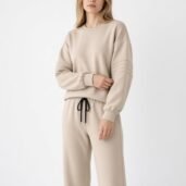 Beige matching sweatshirt and jogger set on a model with drawstring waist and ribbed cuffs, neutral studio backdrop (loungewear photo).