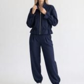 Woman in a navy blue zip-up jogger suit with drawstring waist, standing against a light background, wearing white sneakers.