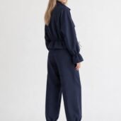 Woman wearing a navy cinched-waist jumpsuit with elastic cuffs, standing in profile in white sneakers.