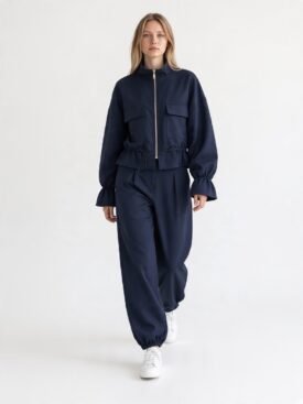 Woman wearing a navy zip-up jacket with large pockets and matching jogger pants, white sneakers, posing against a light background