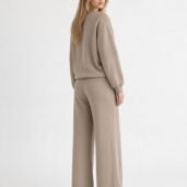 Woman wearing a taupe oversized sweatshirt with matching wide-leg pants, viewed from the back in a studio setting.