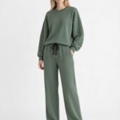 Model wearing a sage green as-looks-like lounge set: oversized sweatshirt with ribbed sleeves and matching wide-leg drawstring pants, white sneakers