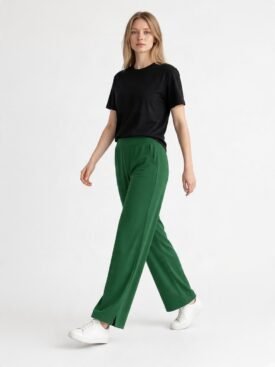 Woman in a black T-shirt and emerald green wide-leg pants walking forward in white sneakers.