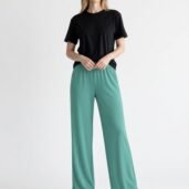 Woman standing in a black t-shirt and teal wide-leg pants, white sneakers, hands at her waistban